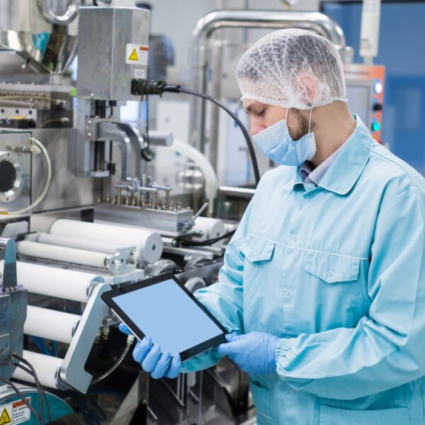 caucasian scientist man in blue lab uniform stand near manufacture machine with shafts, show empty tablet, close picture, focus on tablet, look at tablet
