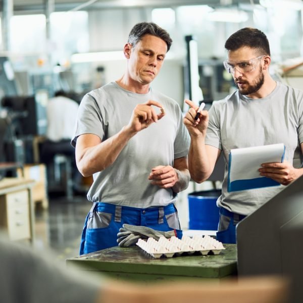 Industrial workers cooperating while doing quality control of manufactured products in a factory.